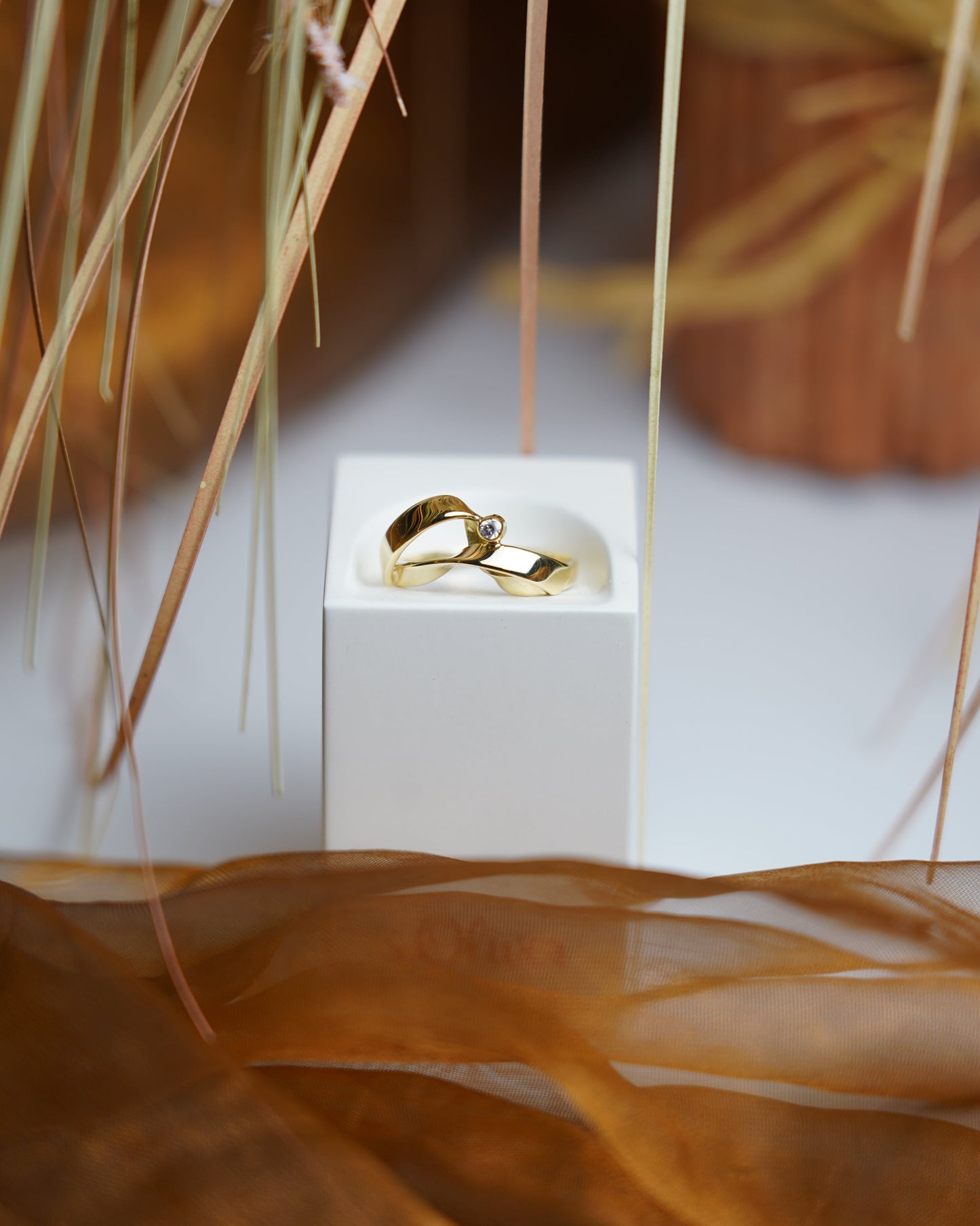Ring Golden Embrace aus 585/- Gelbgold mit geschwungenem Design und einem funkelnden Zirkoniastein auf weißem Schmuckdisplay.