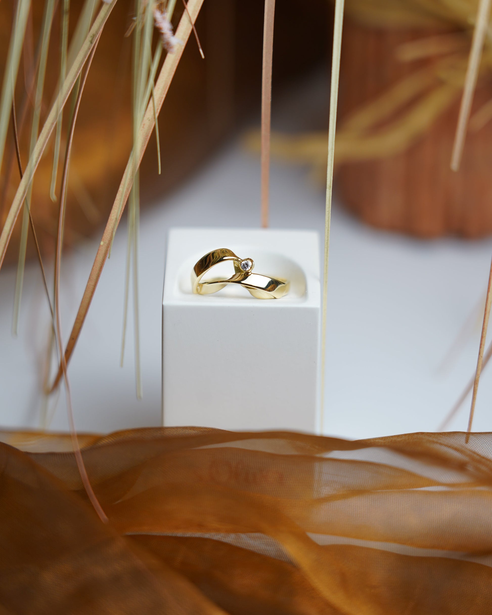 Ring Golden Embrace aus 585/- Gelbgold mit geschwungenem Design und einem funkelnden Zirkoniastein auf weißem Schmuckdisplay.