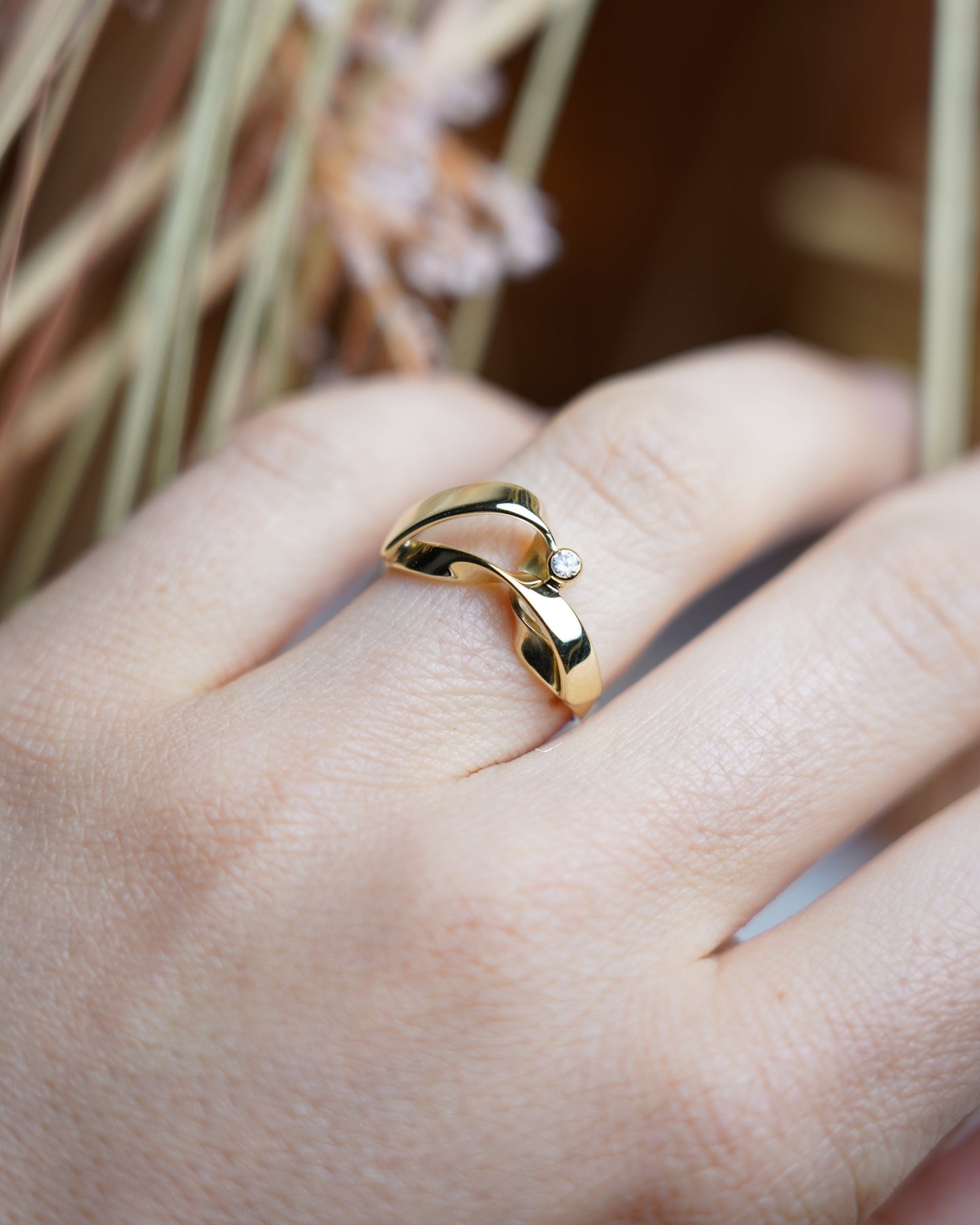 Ring Golden Embrace aus 585/- Gelbgold mit geschwungenem Design und einem funkelnden Zirkoniastein auf weißem Schmuckdisplay.