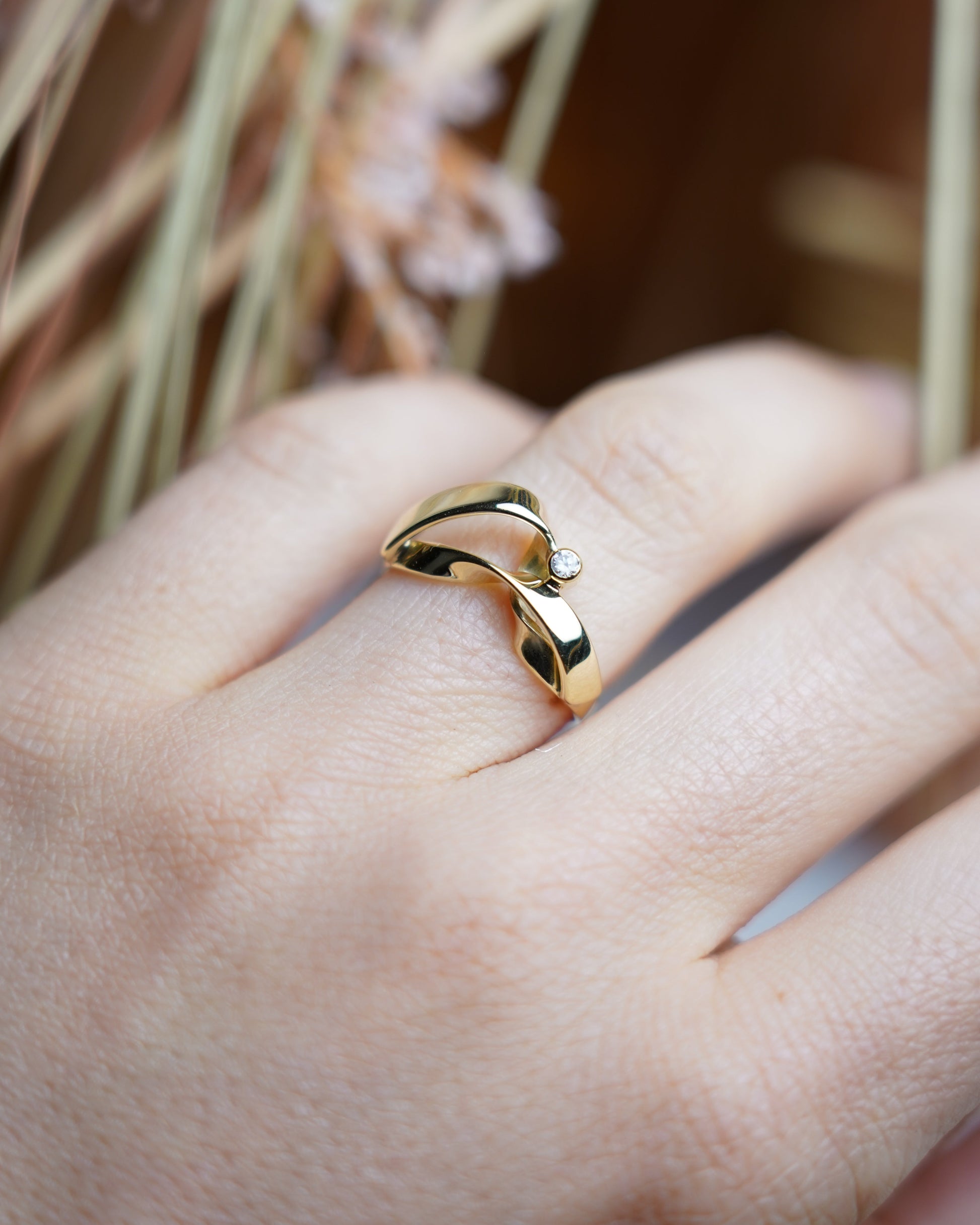 Ring Golden Embrace aus 585/- Gelbgold mit geschwungenem Design und einem funkelnden Zirkoniastein auf weißem Schmuckdisplay.