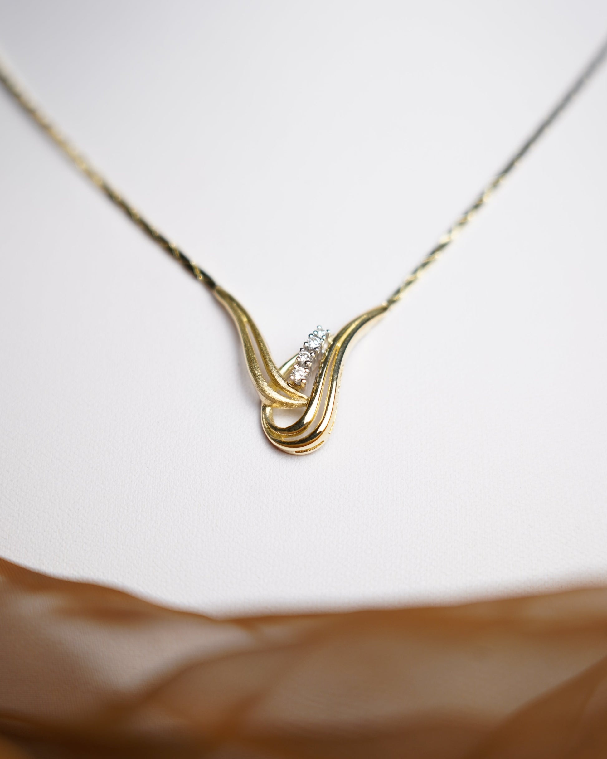 Halskette Golden Harmony aus 585/- Gelbgold mit geschwungenem Anhänger und funkelnden Brillianten auf weißem Schmuckdisplay.